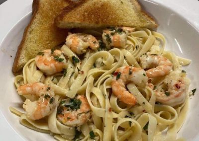 Shrimp scampi pasta with fettuccine noodles, garlic butter sauce, fresh herbs, and toasted bread on white plate