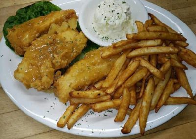 Fish and chips meal with golden battered fish fillets, crispy french fries, tartar sauce, and lettuce on white plate