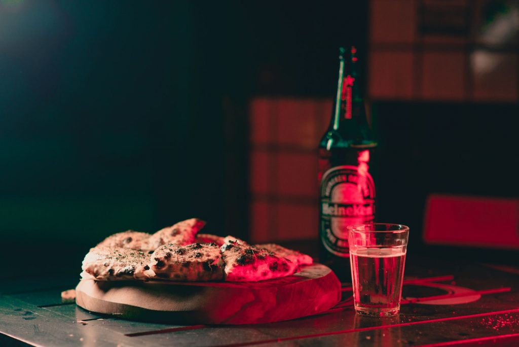 A delicious pizza and beer bottle on a cutting board in warm restaurant lighting ambiance.