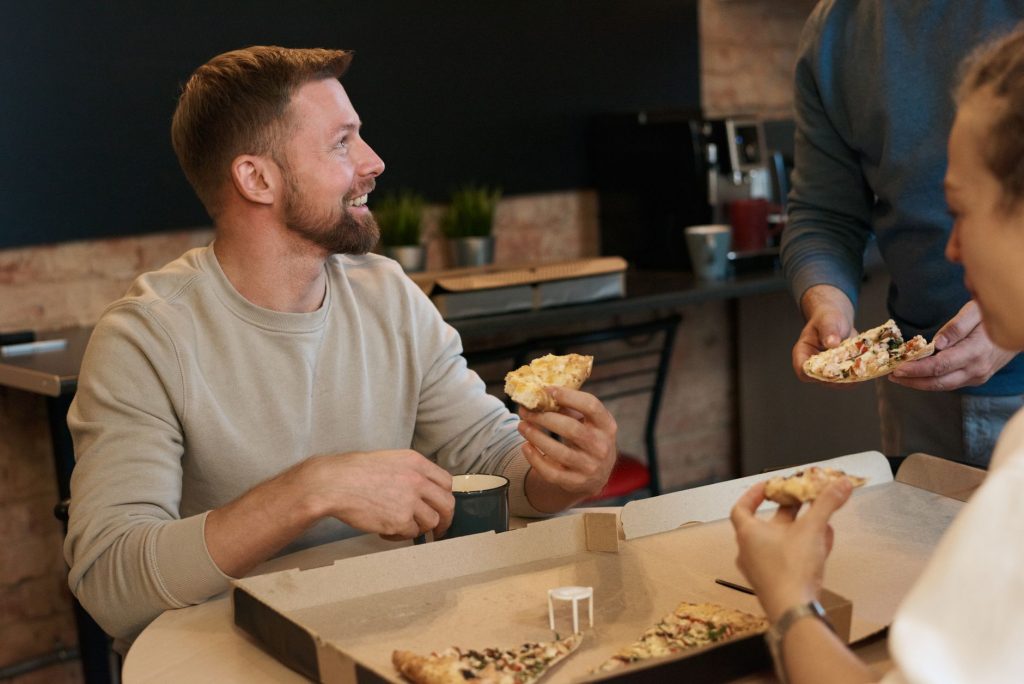 A group of adults enjoying a pizza lunch indoors, smiling and conversing.