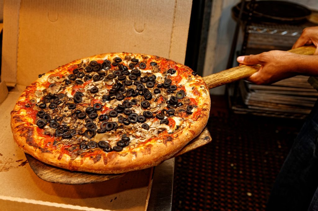 Appetizing pizza with olives and mushrooms being served fresh from the oven.