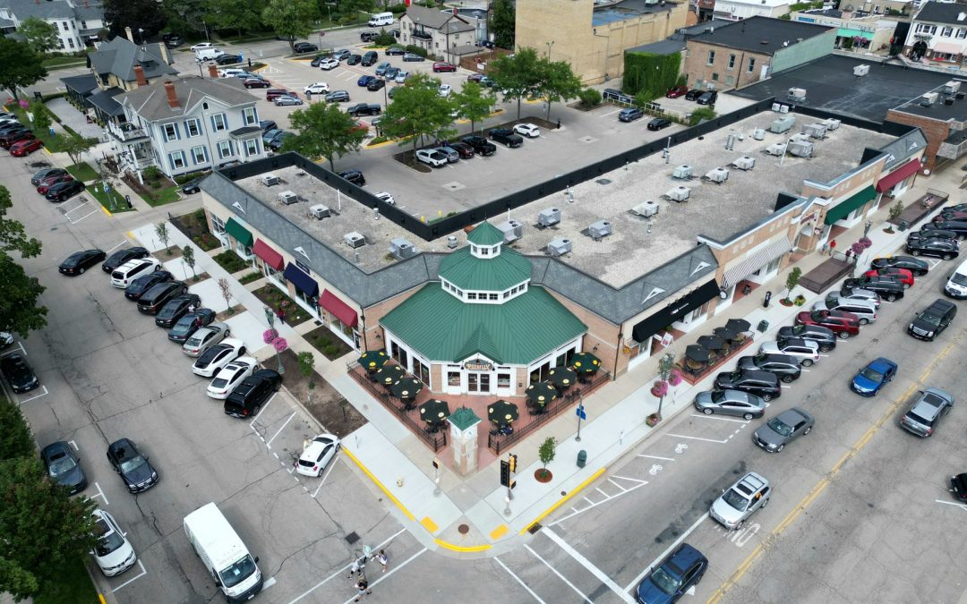 Bird's-eye view of a bustling suburban shopping center with parked cars and tree-lined streets.