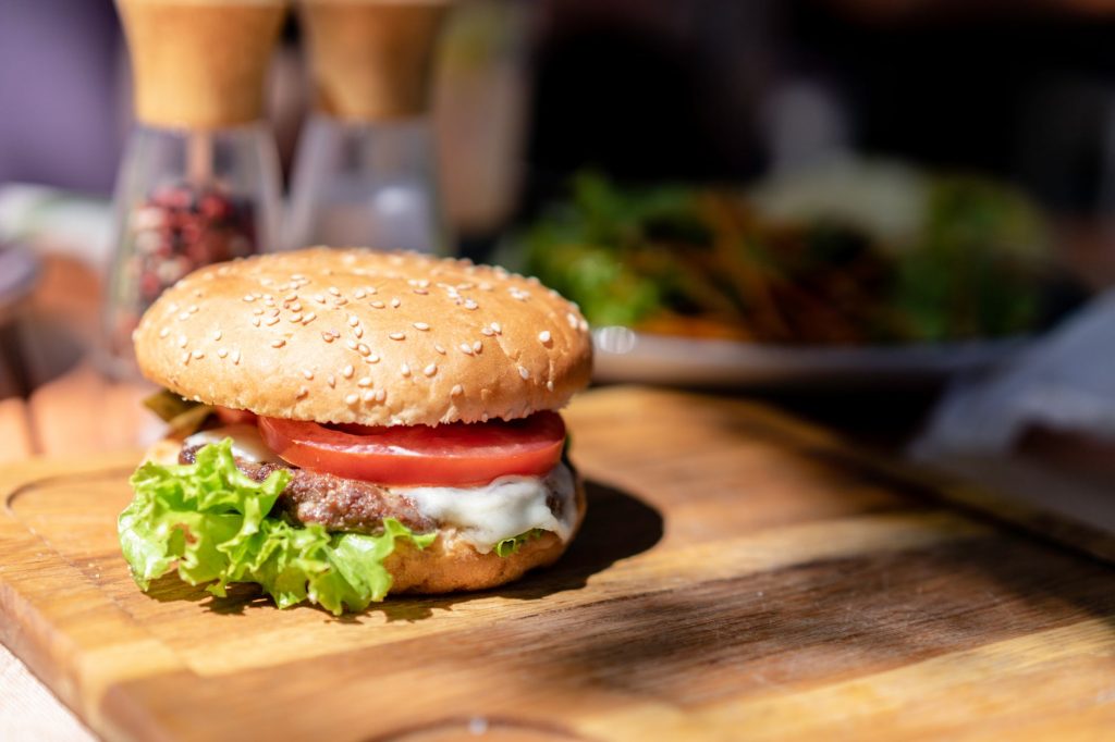 Close-up of a gourmet cheeseburger with lettuce and tomato on a wooden cutting board in natural light.