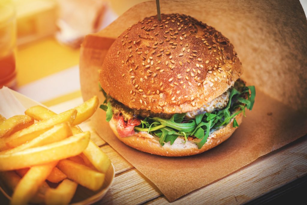 Close-up of a sesame seed bun burger with fresh arugula alongside crispy French fries.