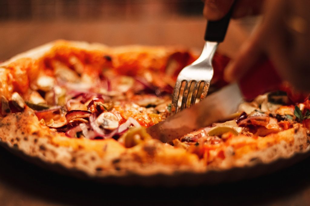 Close-up of a tasty pizza being sliced, featuring fresh ingredients like cheese, onions, and olives.