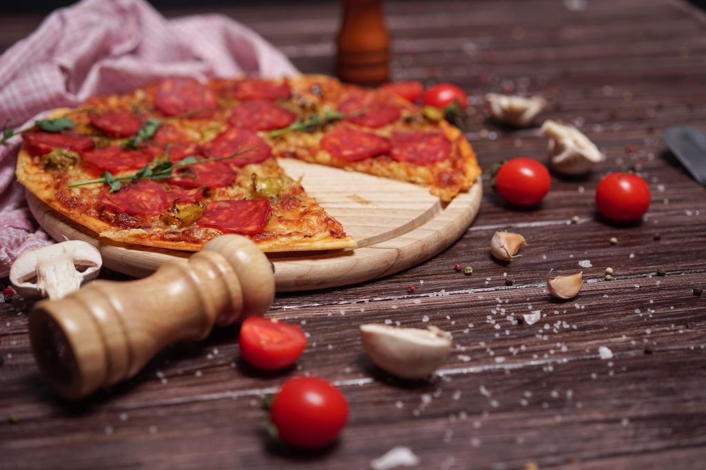 Close-up of pepperoni pizza on a wooden board with cherry tomatoes and garlic cloves on a rustic table.