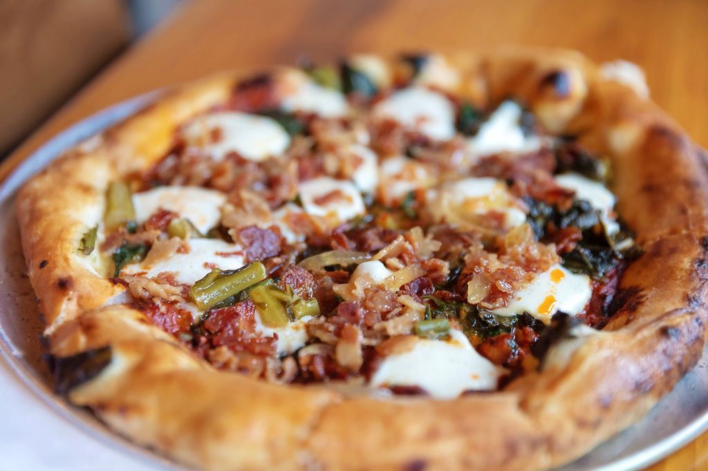 Close-up view of a delicious artisan pizza topped with bacon, cheese, and vegetables on a wooden table.