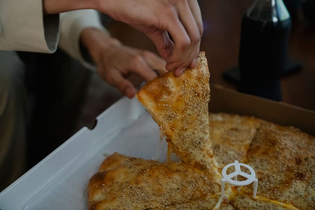 Crop unrecognizable person treating with slice of tasty pizza from carton box spending evening at home