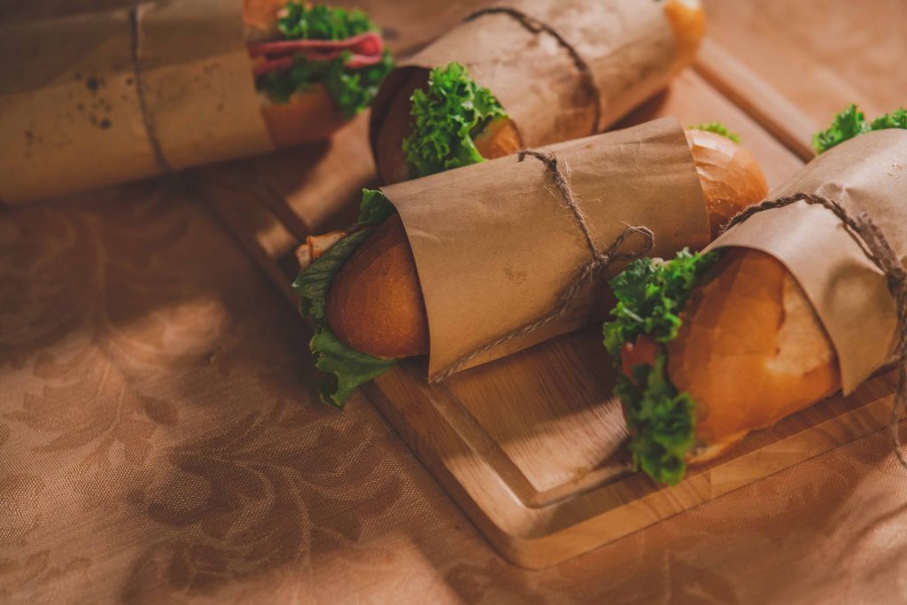 Delicious Banh Mi sandwiches on a wooden board, wrapped in paper, featuring fresh ingredients.