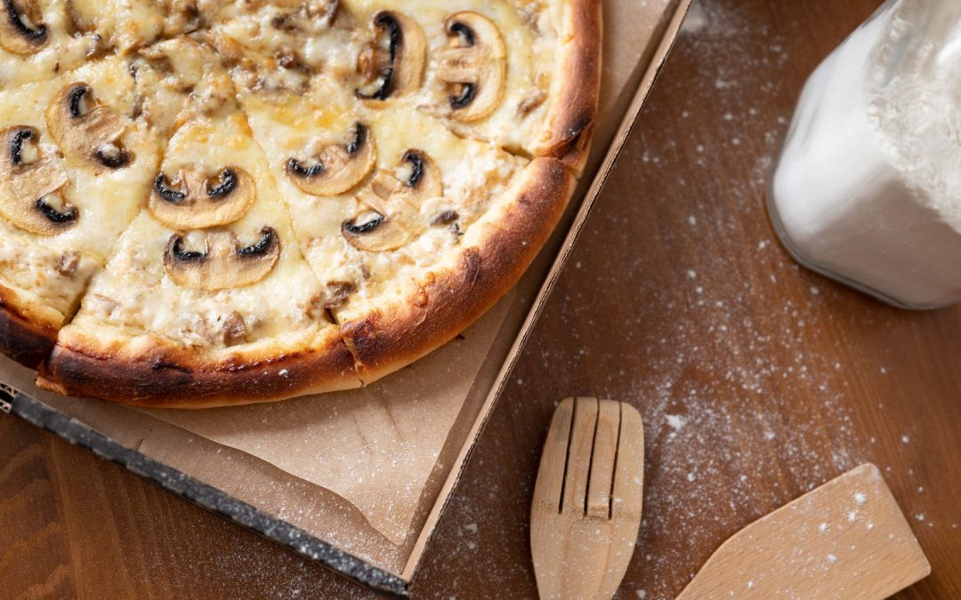 Delicious mushroom pizza with cheese in a cardboard box on a wooden table with flour.