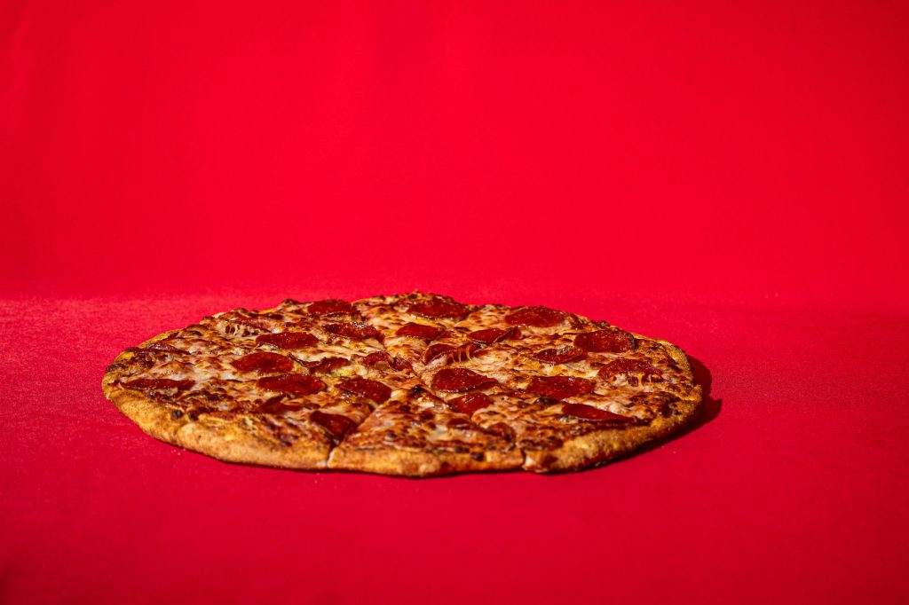 Delicious pepperoni pizza on vibrant red background, perfect for food photography needs.