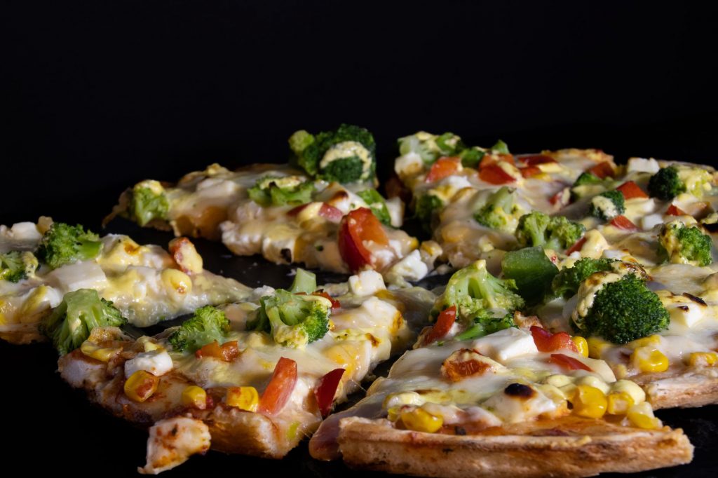 Delicious vegetable pizza with broccoli, cheese, and fresh toppings on a dark background.