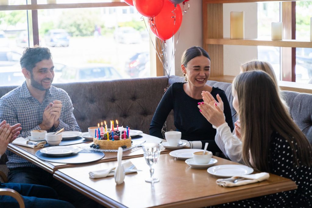 Friends celebrate a birthday with cake and laughter at a cozy restaurant setting.