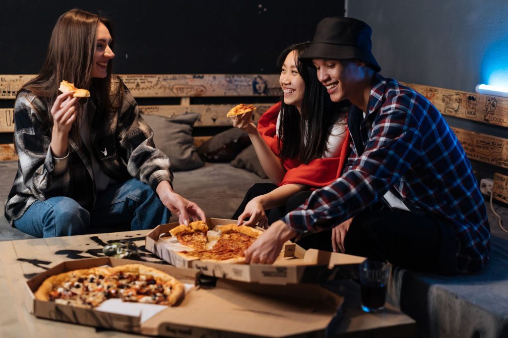 Group of friends enjoying pizza and laughter indoors, creating fond memories.