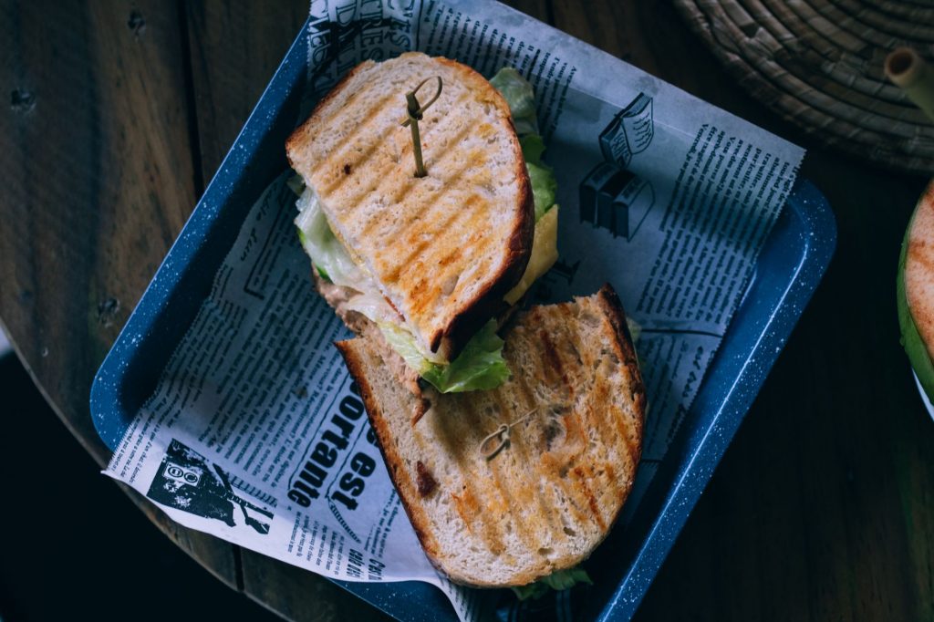 Savory grilled sandwich served on a blue tray with crispy lettuce and newspaper lining.