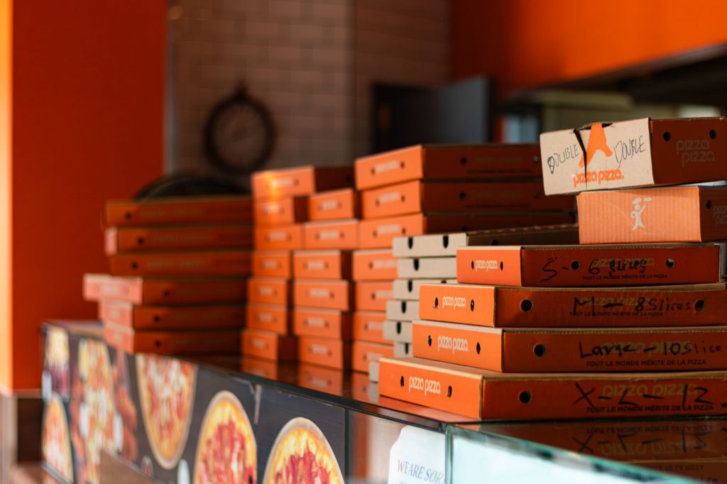 Stacks of bright orange pizza boxes in a Toronto pizzeria against a warm-toned interior.