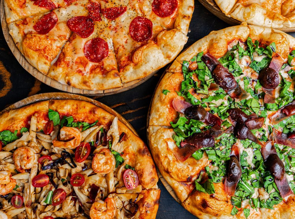 Top view of assorted gourmet pizzas with diverse and colorful toppings, perfect for Italian cuisine lovers.