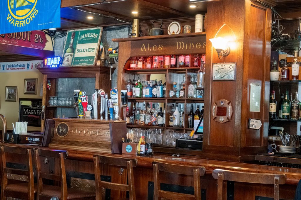 Warm interior of a traditional Irish pub featuring wooden bar and ale signs in San Francisco, CA.