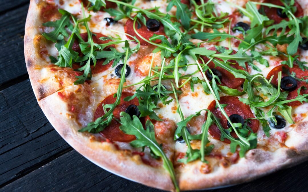 High angle of tasty pizza with black olive rings and fresh herb leaves on melted cheese